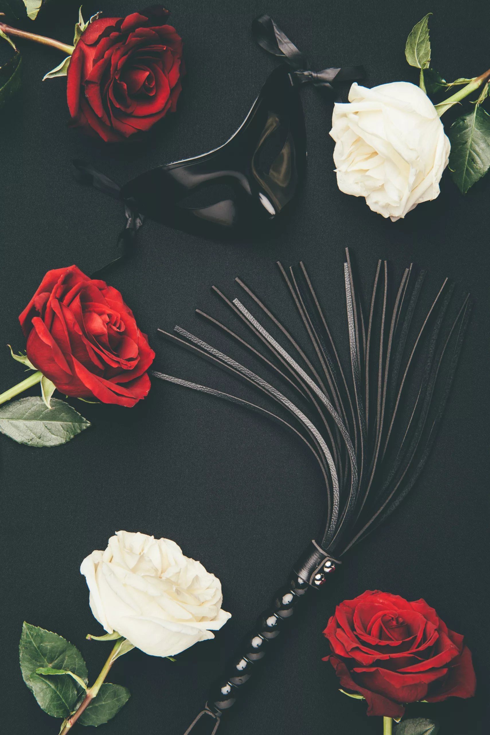 Home black leather whip and mask with rose flowers isolated on black